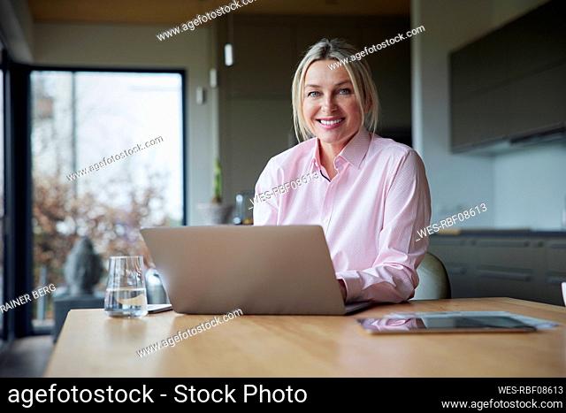 Happy blond woman sitting with laptop at table