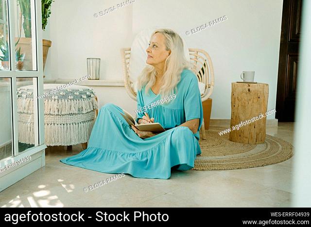 Thoughtful woman sitting with book on carpet at home