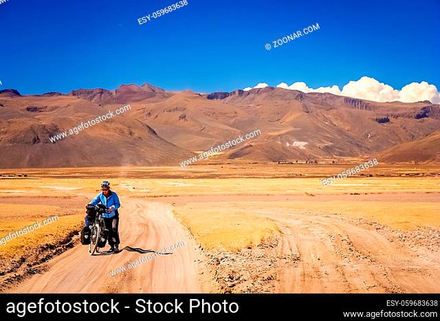 Woman cyclist struggling and pushing her bike on the sandy corrugated road in Altiplano in Bolivia