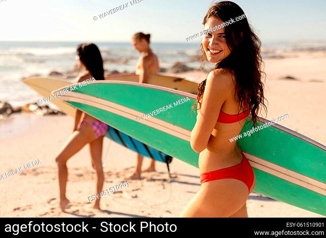 Mixed race people holding surf board on beach