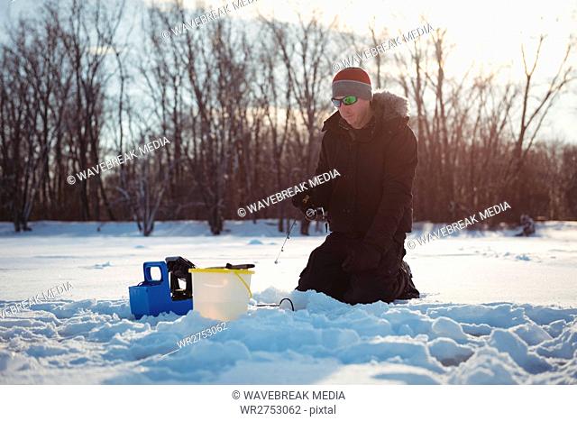 Ice fisherman fishing in snowy landscape
