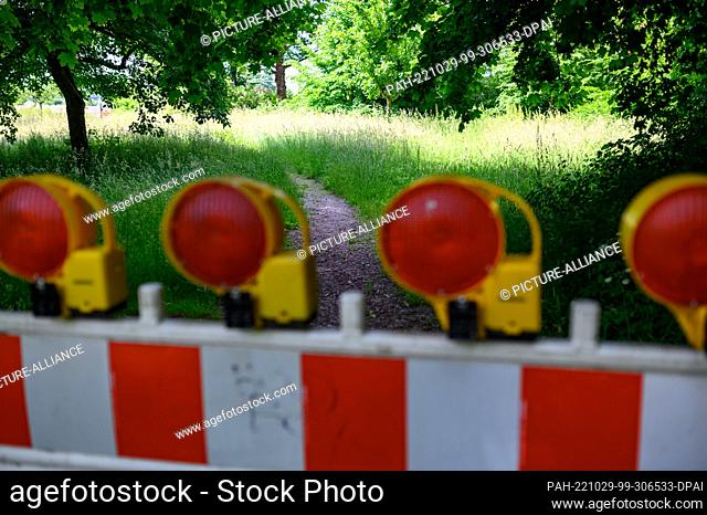 11 June 2022, Hamburg: A construction site barrier stands in front of a trail in a green meadow under trees in Jenischpark. Photo: Jonas Walzberg/dpa
