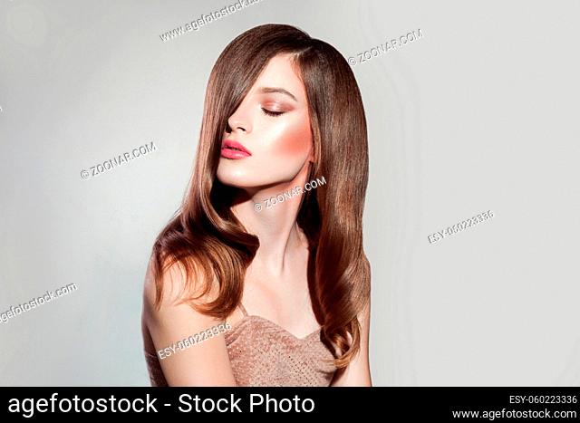 portrait of attractive brunette woman with makeup and straight shiny hairs, closed eyes posing on isolated grey background