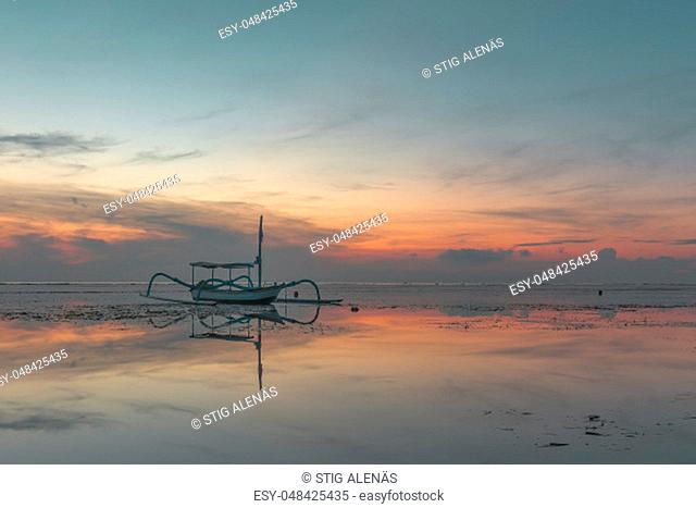 A small indonesian fishing boat at sunrise, reflections in the water, Sanur, Bali, Indonesia, April 21, 2018