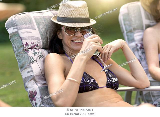 Mature woman wearing bikini, relaxing on sun lounger, drinking wine