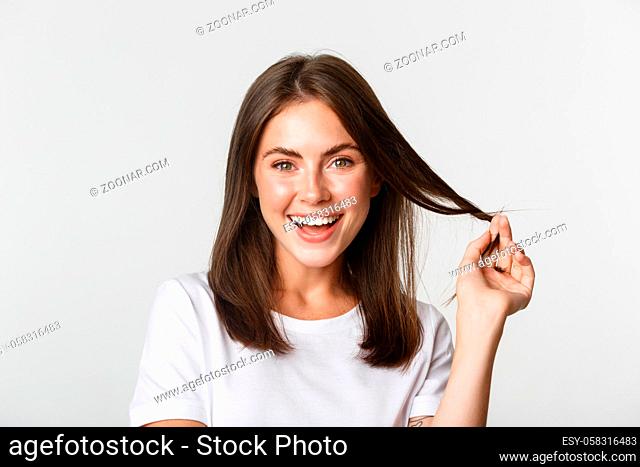 Portrait of flirty beautiful girl playing with hair and smiling at camera intrigued