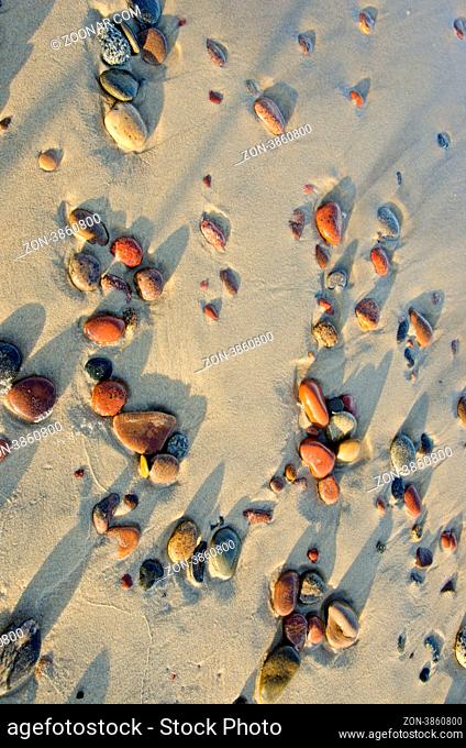 Colorful wet pebbles rubed by waves lying in sea sand