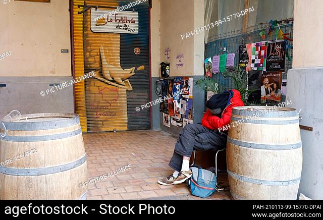 13 January 2021, Spain, Palma de Mallorca: A homeless man sleeps outside a closed tortilla shop amid the ongoing Corona pandemic. Since 13.01