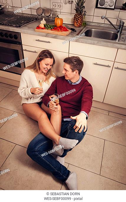 Young couple sitting on kitchen floor and drinking champagne
