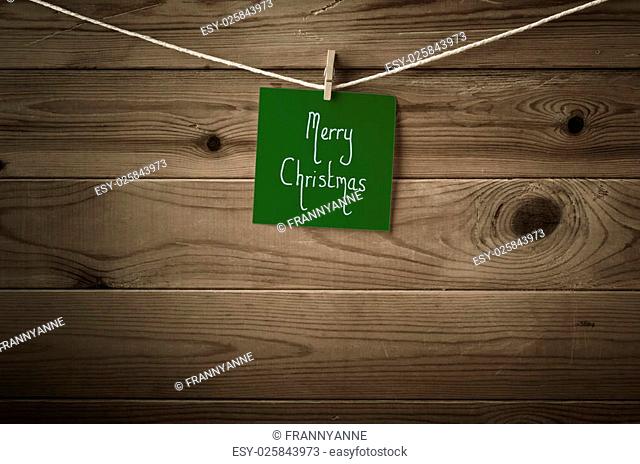 Merry Christmas message written on a square of festive dark green note paper and pegged to a string washing line, Wood plank fence background
