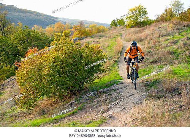 Cyclist in Orange Riding the Mountain Bike on the Autumn Rocky Enduro Trail. Extreme Sport and Enduro Biking Concept