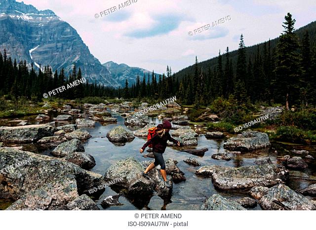 Side view of mid adult woman walking on rocky riverbed, Moraine lake, Banff National Park, Alberta Canada