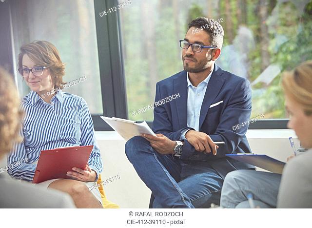 Attentive man with clipboard listening in group therapy session