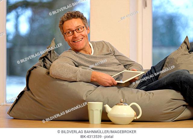 Man lying on large pillow with tablet, iPad, Germany