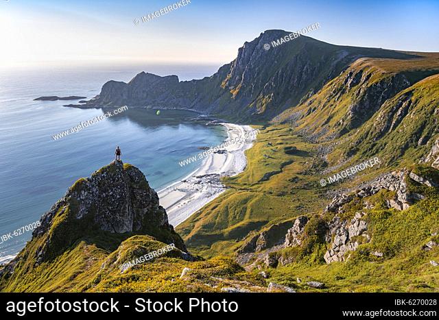 Hiker on rocks, cliffs, beach and sea, behind summit of mountain Måtinden, near Stave, Nordland, Norway, Europe