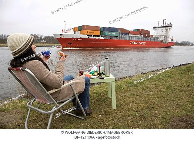 Young woman, 30-35 years, having breakfast on a damp winter day at the Kiel Canal, watching passing ships, Schleswig-Holstein, Germany, Europe