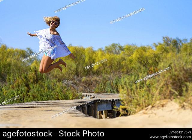Carefree woman jumping barefoot in air on elevated footbridge leading towards natural forest. Crazy woman jumping on elevated bridge leading into woods