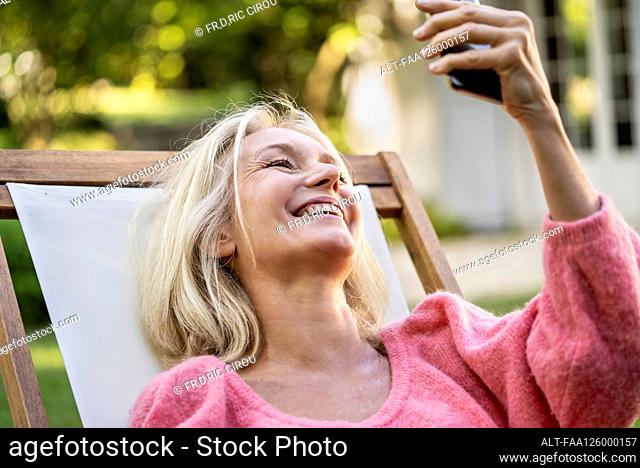 Close-up of smiling mature woman having video call on smartphone in backyard
