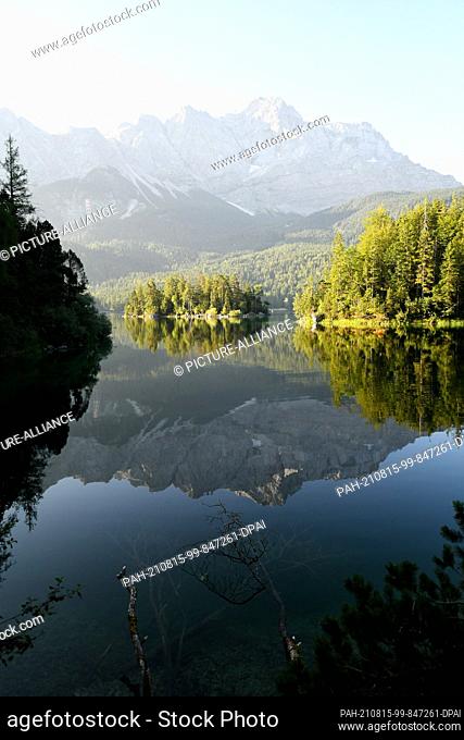 15 August 2021, Bavaria, Grainau: The Zugspitze (M) is reflected in the still smooth surface of the Eibsee. Photo: Angelika Warmuth/dpa