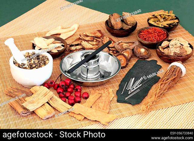 Traditional Chinese herbs used in herbal medicine with acupuncture needles and moxa stick used in moxibustion therapy on bamboo mats and green background