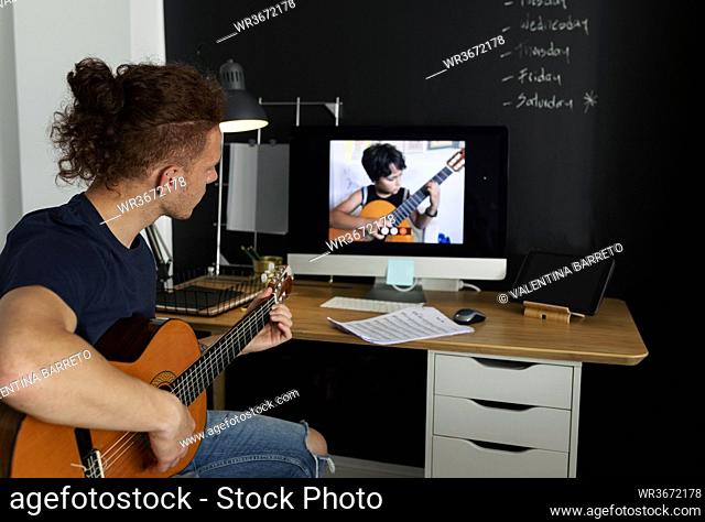 Man learning guitar while watching tutorial at home