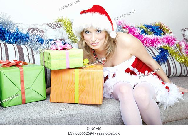 Smiling lady in Santa Claus costume sitting indoors near the Christmas gifts