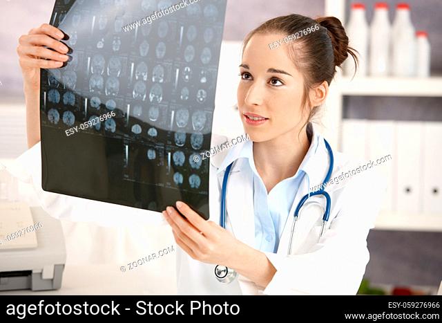 Young female doctor sitting at desk in doctor's room looking at x-ray image