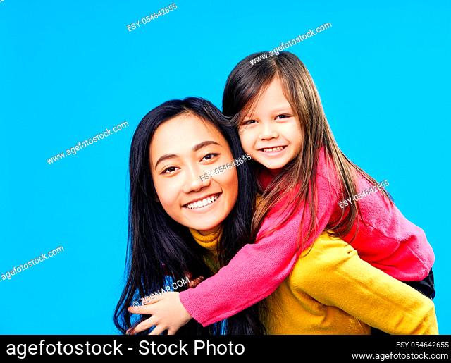 Happy mother and little daughter piggybacking together isolated on blue background. Family concept