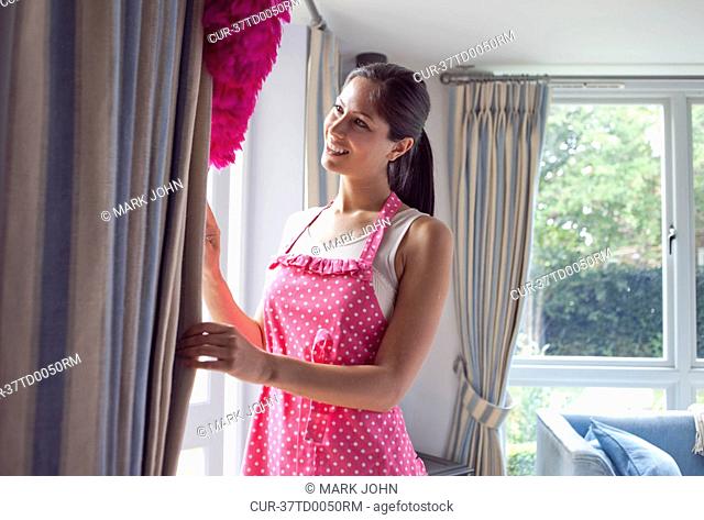 Woman dusting curtains in living room