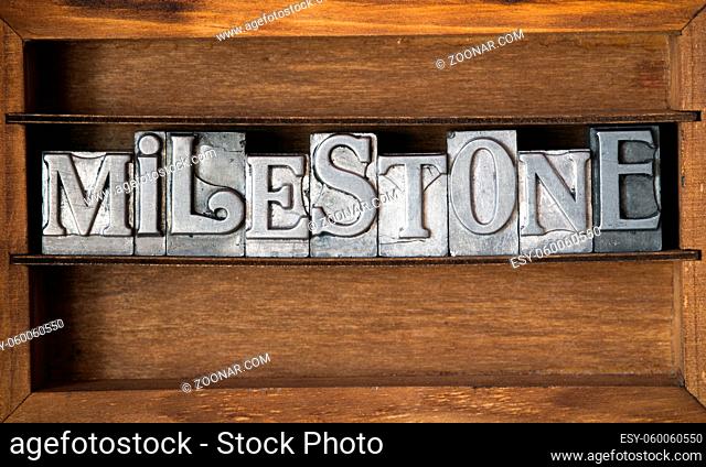 milestone word made from metallic letterpress type on wooden tray