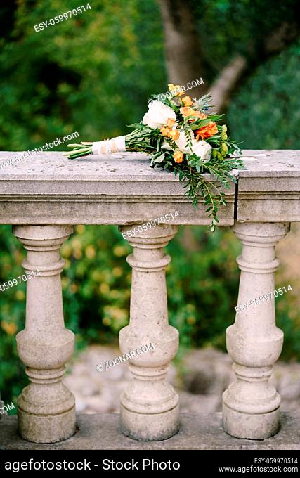bridal bouquet of white and orange roses, eringyum, ammi, boxwood branches, alstroemeria with white ribbons on the railing of an ancient staircase
