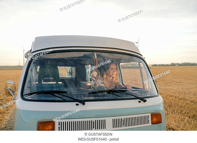 Smiling young woman driving camper van in rural landscape