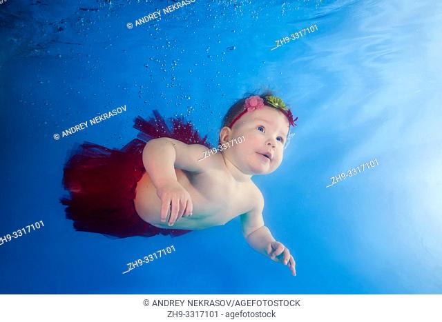 Funny face portrait of baby girl in a red skirt swimming and diving underwater with fun in the pool. Healthy family lifestyle and children water sports activity