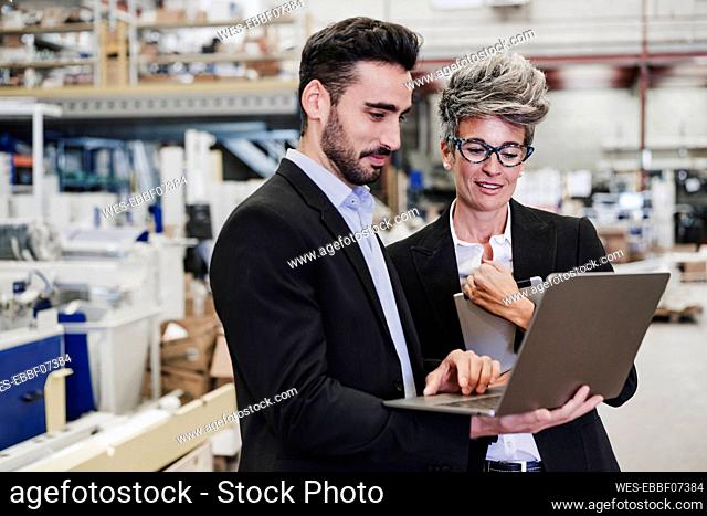 Happy mature businessman discussing with colleague over laptop in industry