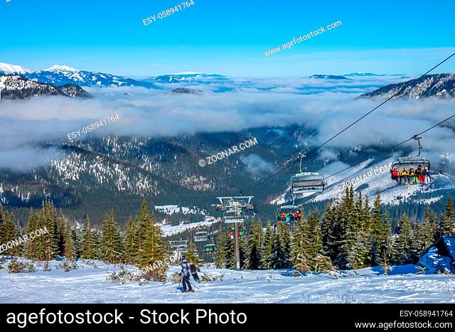 Slovak ski resort Jasna. Snow glistens in the sun. Blue sky and light fog between the mountain peaks. Chair ski lift and skiers
