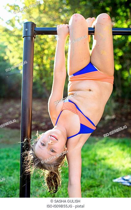 Portrait of girl in bikini upside down on garden climbing frame