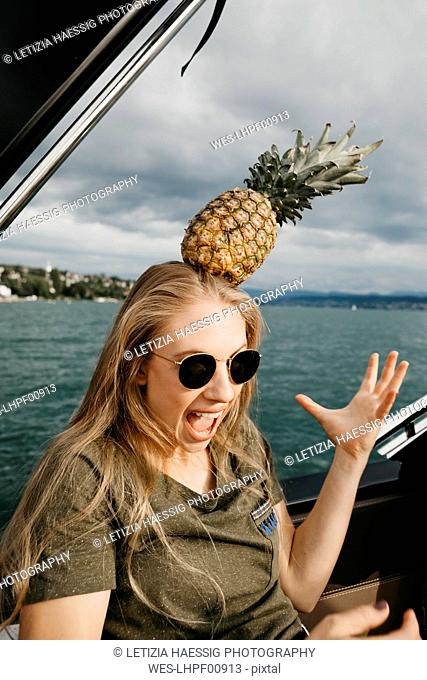 Screaming young woman on a boat balancing a pineapple on her head