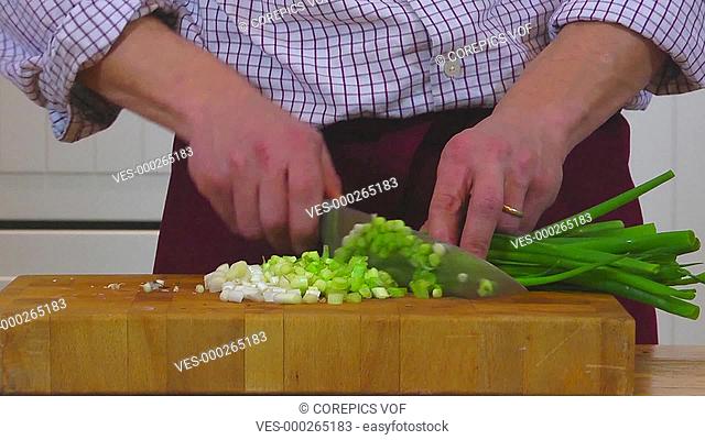 Frontal shot of a home chef cutting spring unions with a kitchen knife on a wooden cutting board