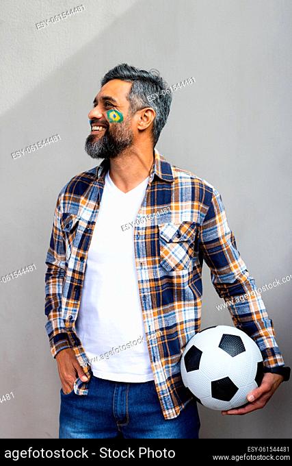 Happy biracial man with football and flag of brazil on his cheek