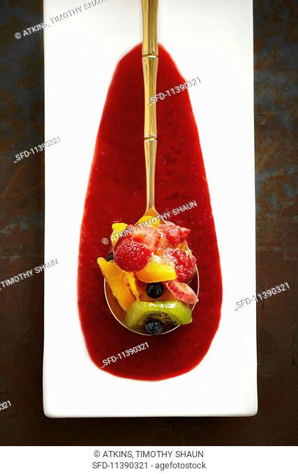 Fruit salad served on a golden spoon in a pool of sauce (seen from above)