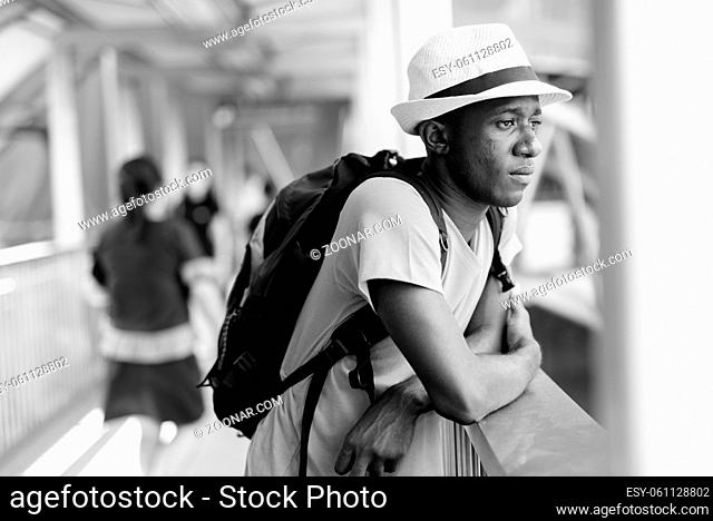 Portrait of young African tourist man as backpacker exploring the city of Bangkok in black and white