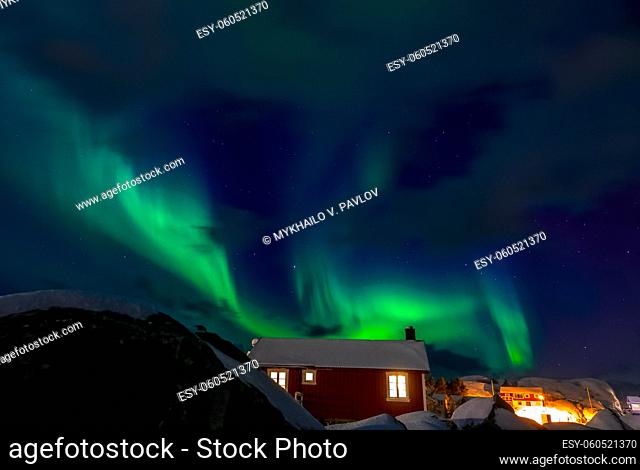 Norway. Winter night on the Lofoten Islands. Aurora borealis and glowing windows of authentic Norwegian houses
