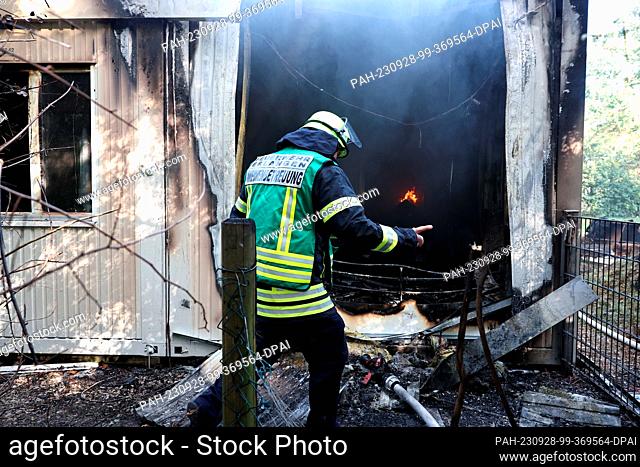 28 September 2023, Bavaria, Erlangen: A firefighter works in the smoking debris of a refugee shelter. The shelter consists of several containers