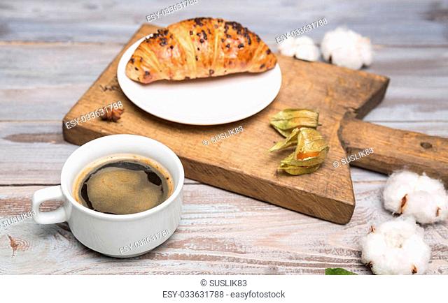 chocolate croissant and a cup of coffee and cotton flowers on a wooden background