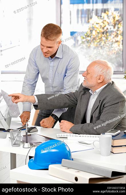 Senior and junior designers discussing work together in office, senior man pointing at screen