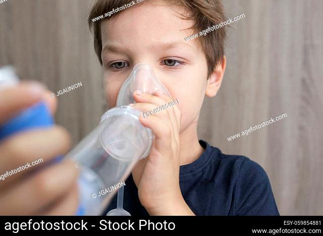 Child boy using medical spray for breath. Inhaler, spacer and mask. Side view
