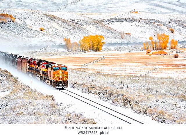 Train transporting tank cars. Season changing, first snow and autumn trees. Rocky Mountains, Colorado, USA