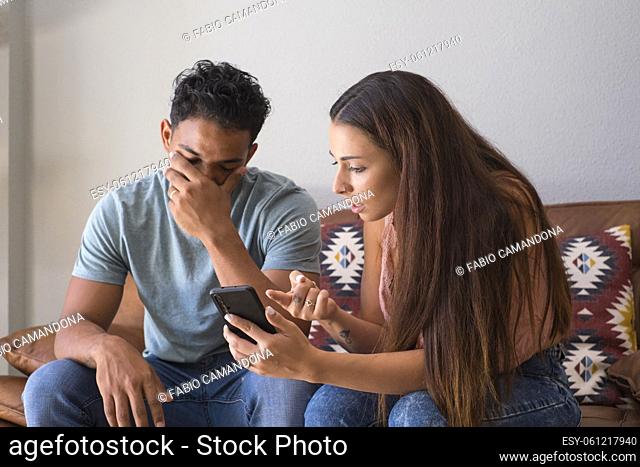 Infidelity. Jealous girlfriend Showing his Cheating boyfriend his Phone Demanding Explanation Sitting On Sofa Indoor at home