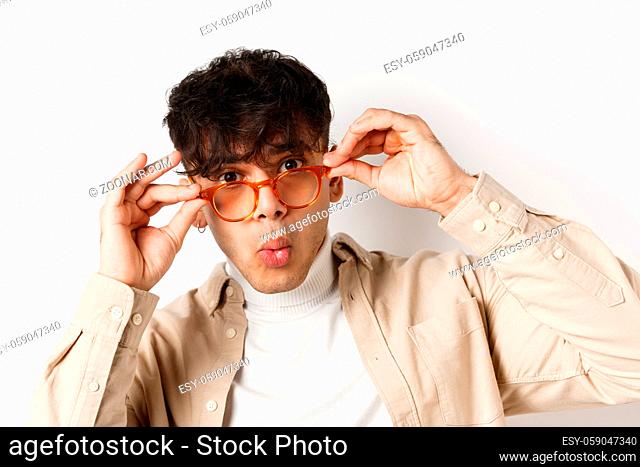 Close-up of attractive young man checking out something cool, look under glasses and saying wow amazed, stare at awesome promo, white background