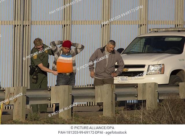 02 December 2018, US, ---: US border officials are searching a migrant, ..after crossing the border fence between Mexico and the United States
